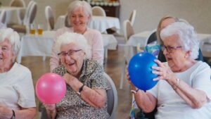 Older adults seated together making seasonal crafts near a bright window with plants and art supplies.
